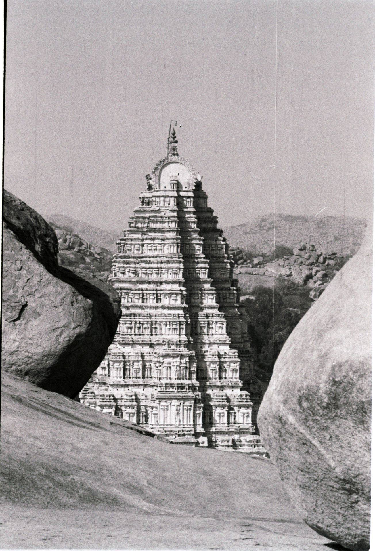 Black-and-white film photograph of the Virupaksha temple tower in Hampi, framed between two large granite boulders.