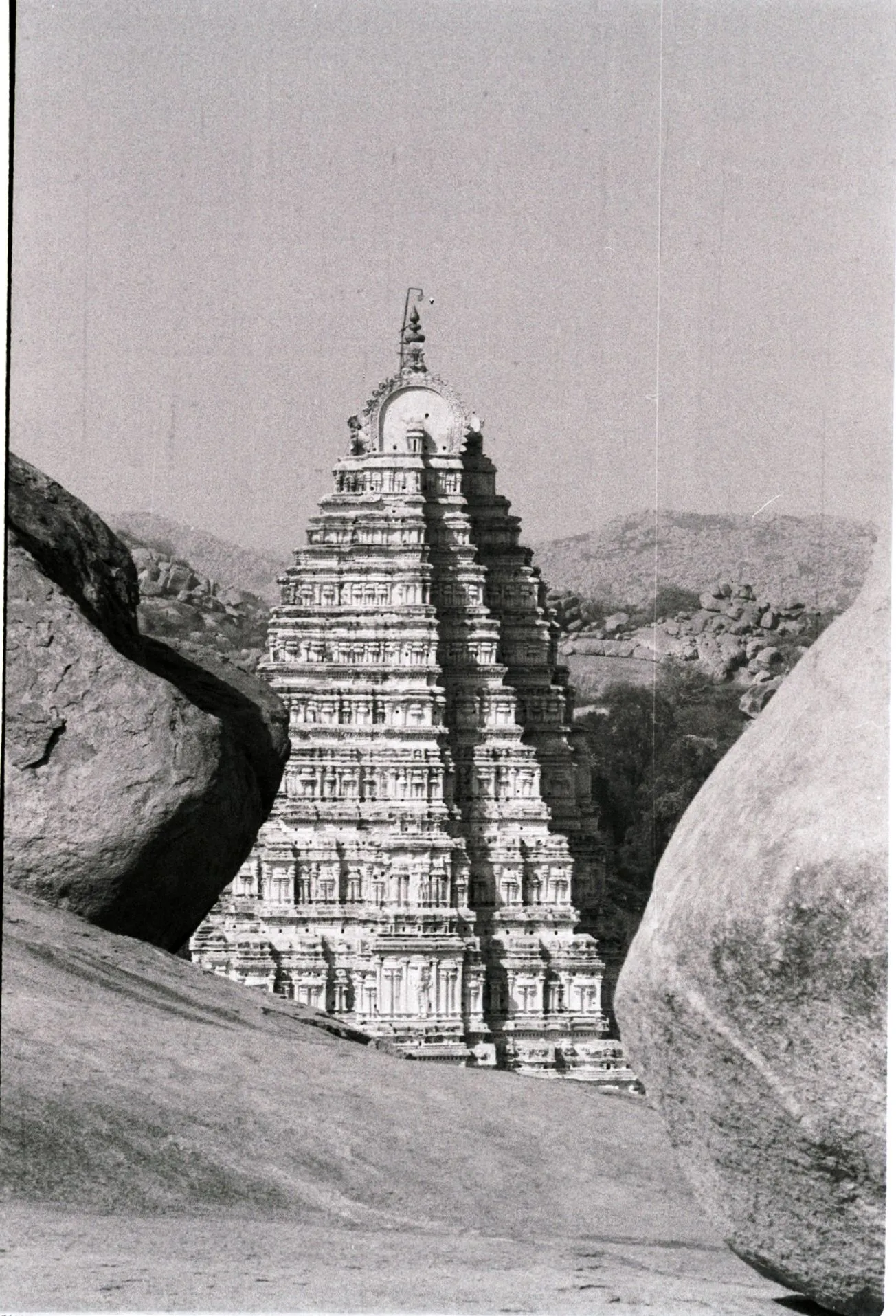 Black-and-white film photograph of an Indian temple tower framed between large stone boulders.